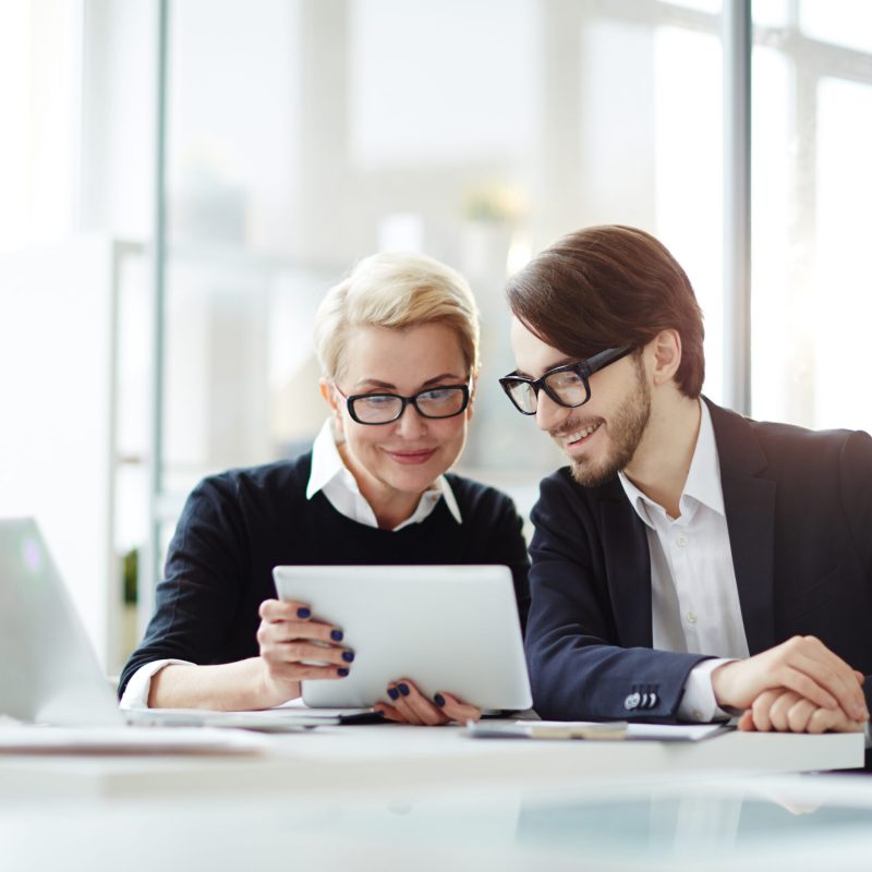 Contemporary employees with digital tablet watching video conference or online seminar while sitting in office